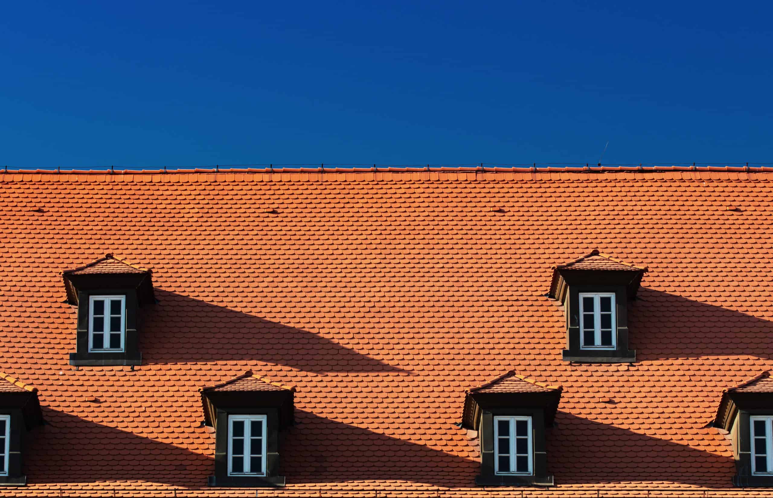 A red tiled roof with two windows and a blue sky.
